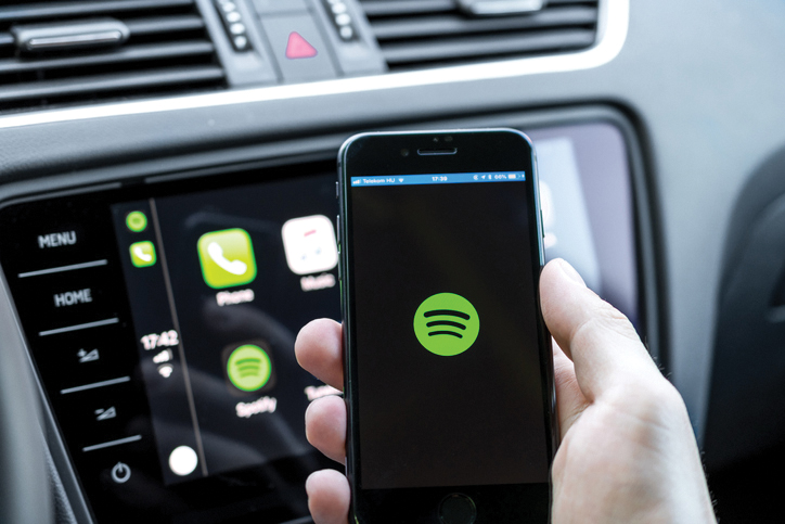 Male hands holding a smartphone that is connecting to the car’s computer running the popular music streaming service