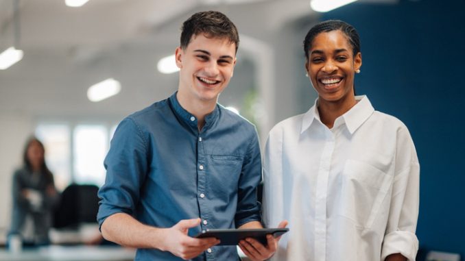 Two young happy business colleagues smiling at the camera holding a digital tablet